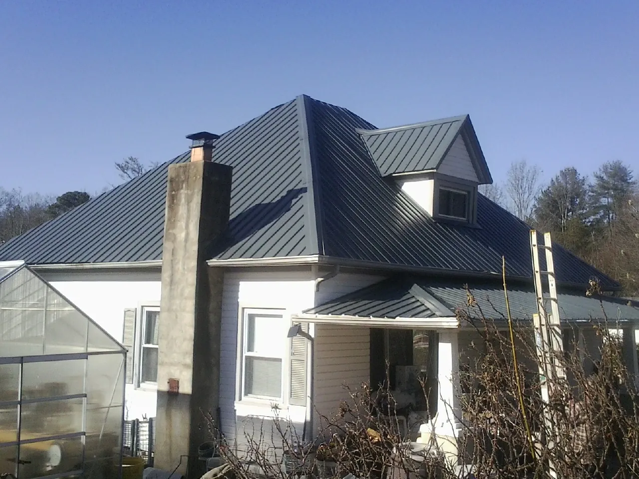 Dark blue standing seam metal roof on a white farmhouse with dormer — Slate & Tile Roof Repair by Roofing Brothers in Bogota