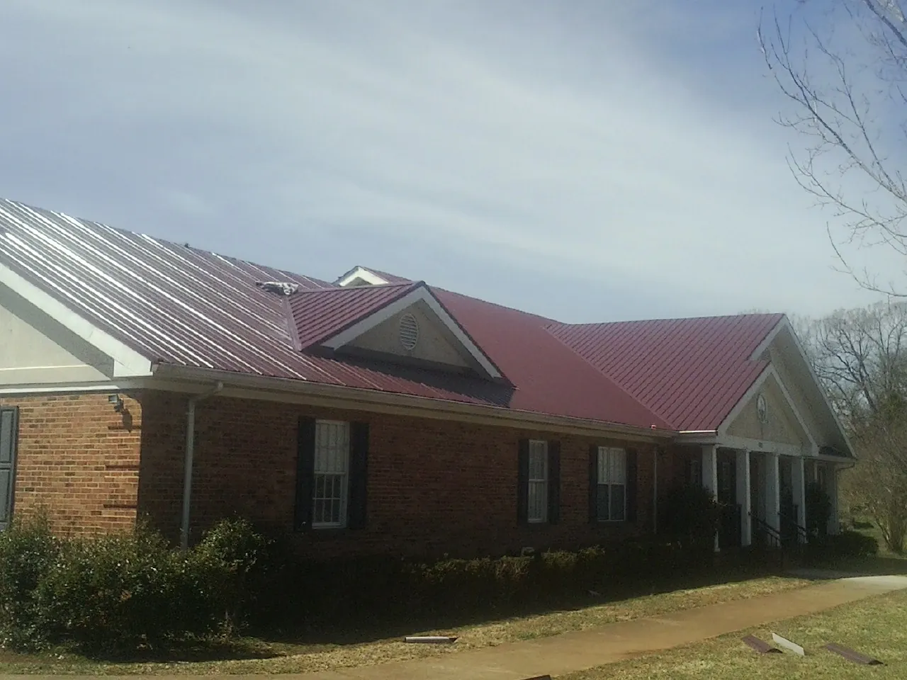 Red metal roof with gabled entries on a long brick building, from a Hail Damage Roof Repair job in Bogota