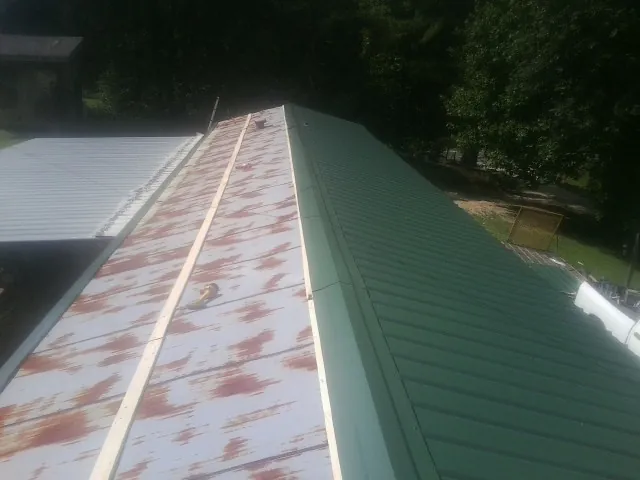 Old rusted panels beside newly installed green metal roofing — Wind Damage Roof Repair by Roofing Brothers in Bogota