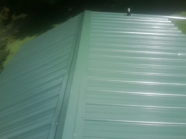 New green metal panels meeting at the ridge of a roof — Flat Roof Repair work by our crew in Bogota
