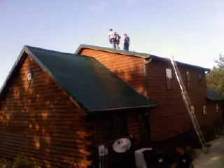 Crew on the ridge of a green metal roof on a two story log home in Bogota