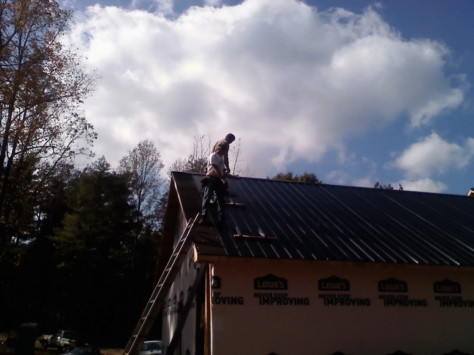 Roofer fastening dark metal panels high against a cloudy sky, from a Roof Inspection job in Bogota