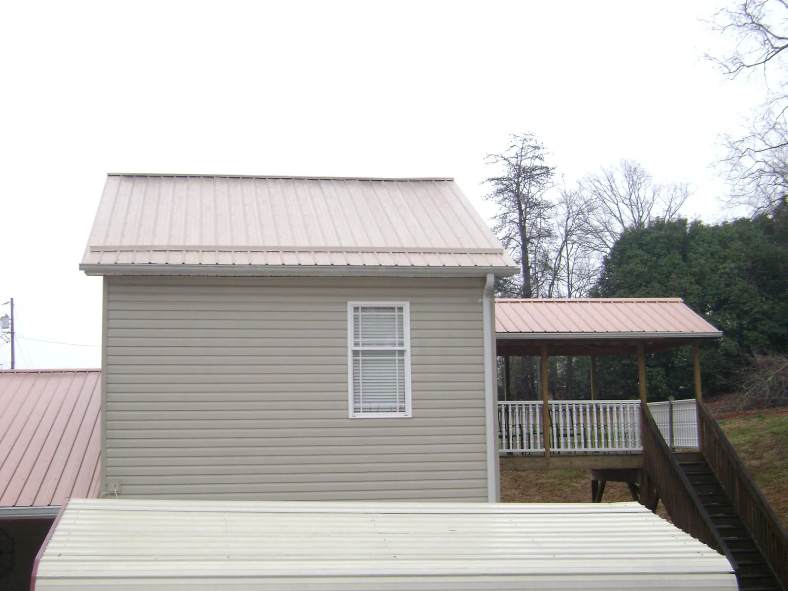 Tan metal roofs on a two story addition and attached porch, from a Roof Replacement job in Bogota